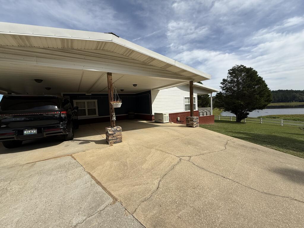 Home with a broad covered carport and driveway, with water visible beyond the lawn.