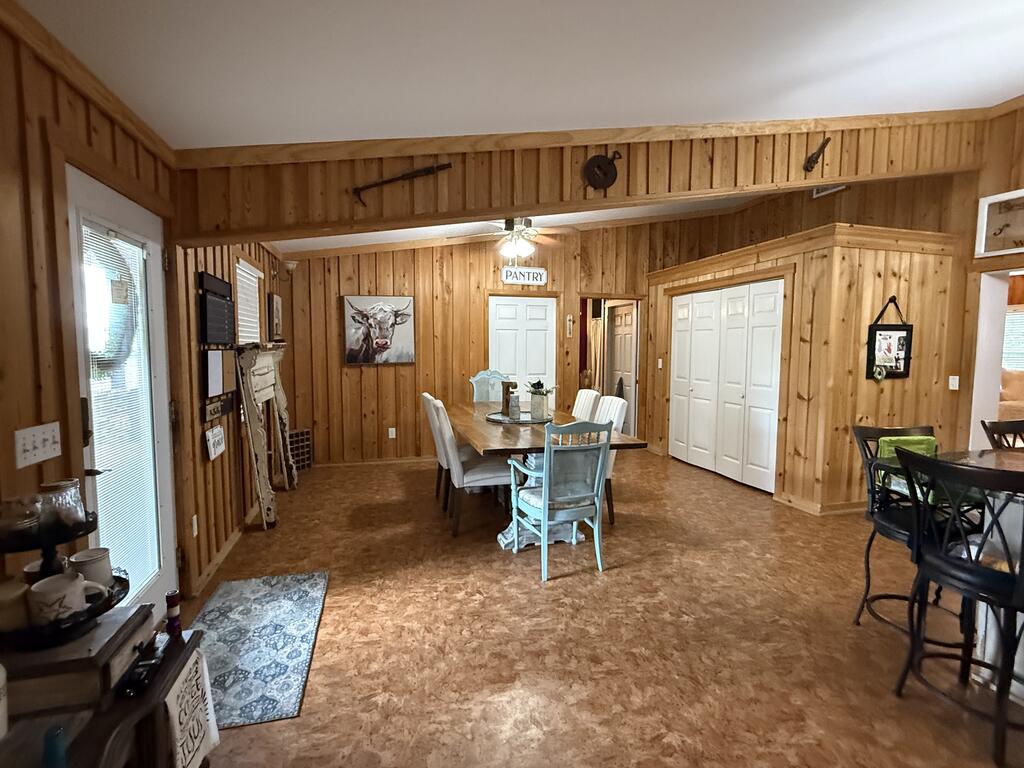 Wood-paneled dining area with a long table, white pantry doors, and a ceiling fan.
