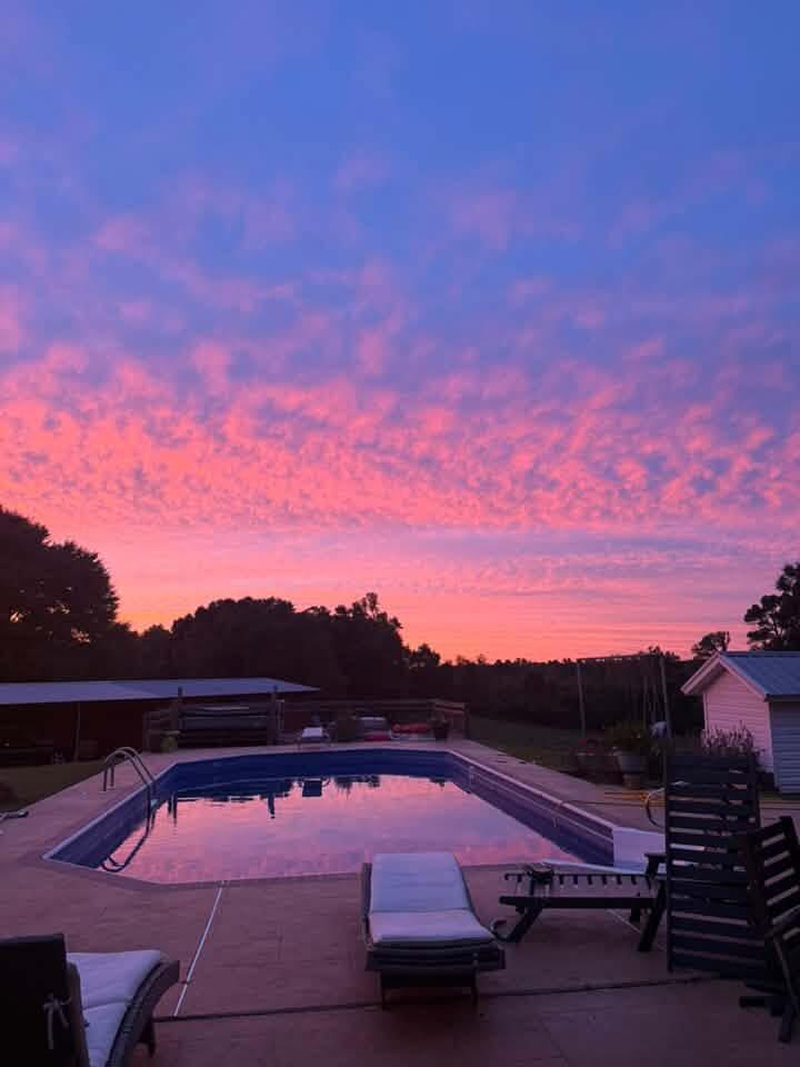 Swimming pool at dusk, reflecting a pink sunset beside a patio with lounge chairs.