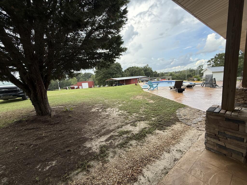 Backyard with a swimming pool and patio seating, viewed from beneath a covered porch.