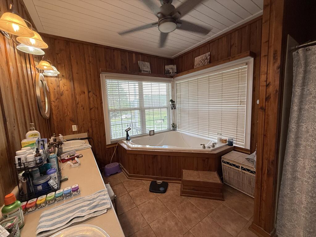 Wood-paneled bathroom with a corner soaking tub beneath wide windows and a long vanity.