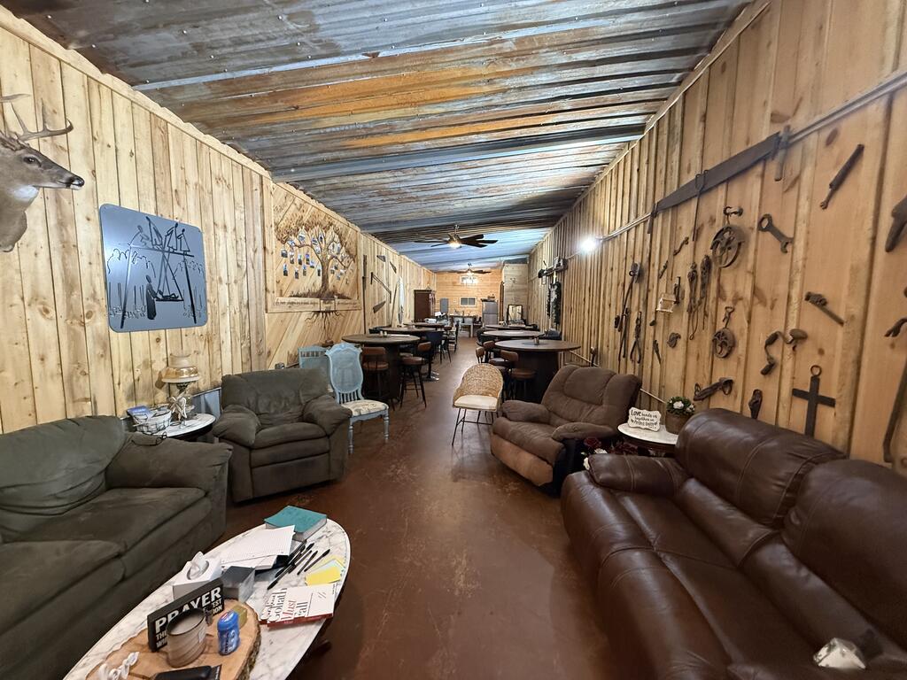 Long rustic room with sofas, tables, and mounted tools along wood-plank walls.