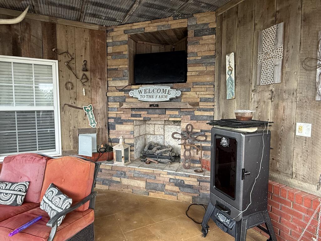 Rustic covered sitting area with a stone fireplace, wood-burning stove, and red cushioned seating.