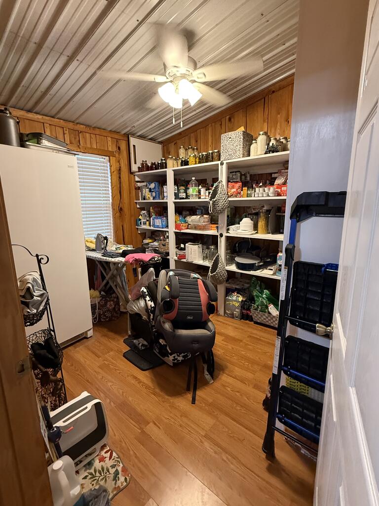 Pantry with stocked open shelves, a white refrigerator, wood-paneled walls, and a ceiling fan.