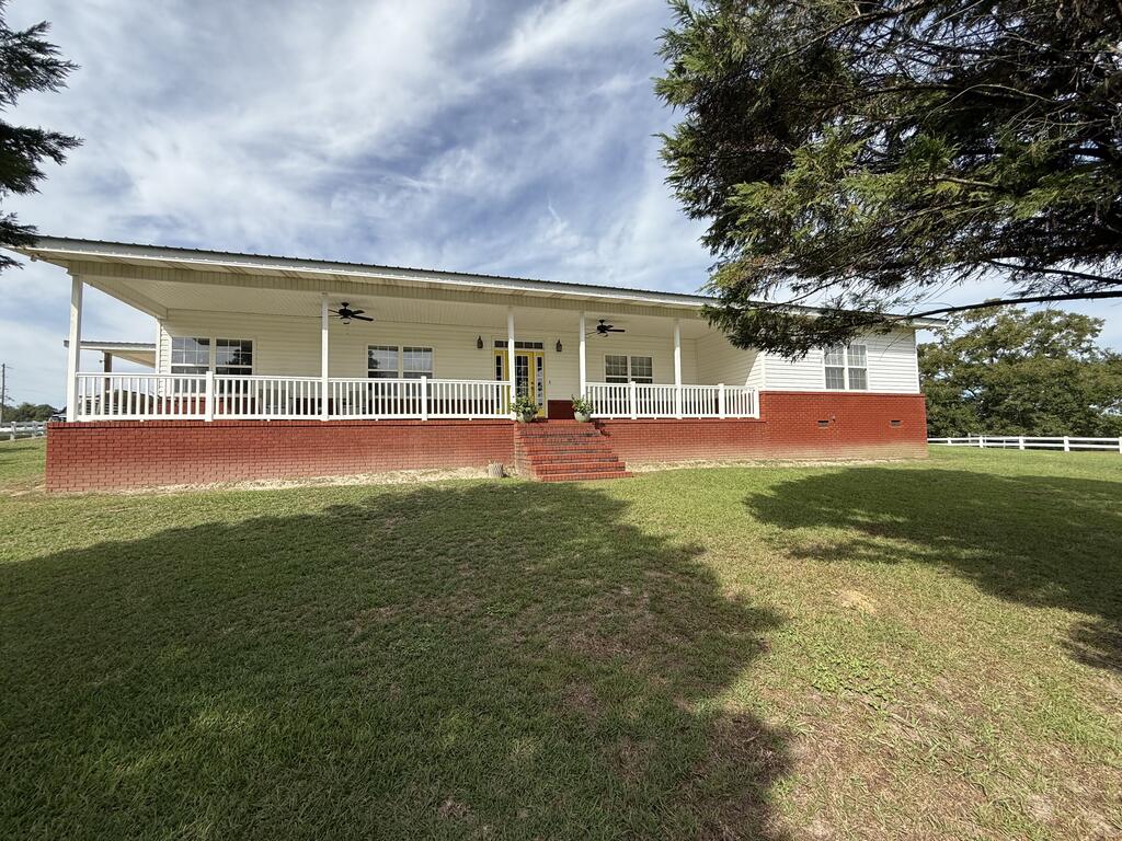 Single-story home with a long white-railed porch, brick foundation, and broad lawn.