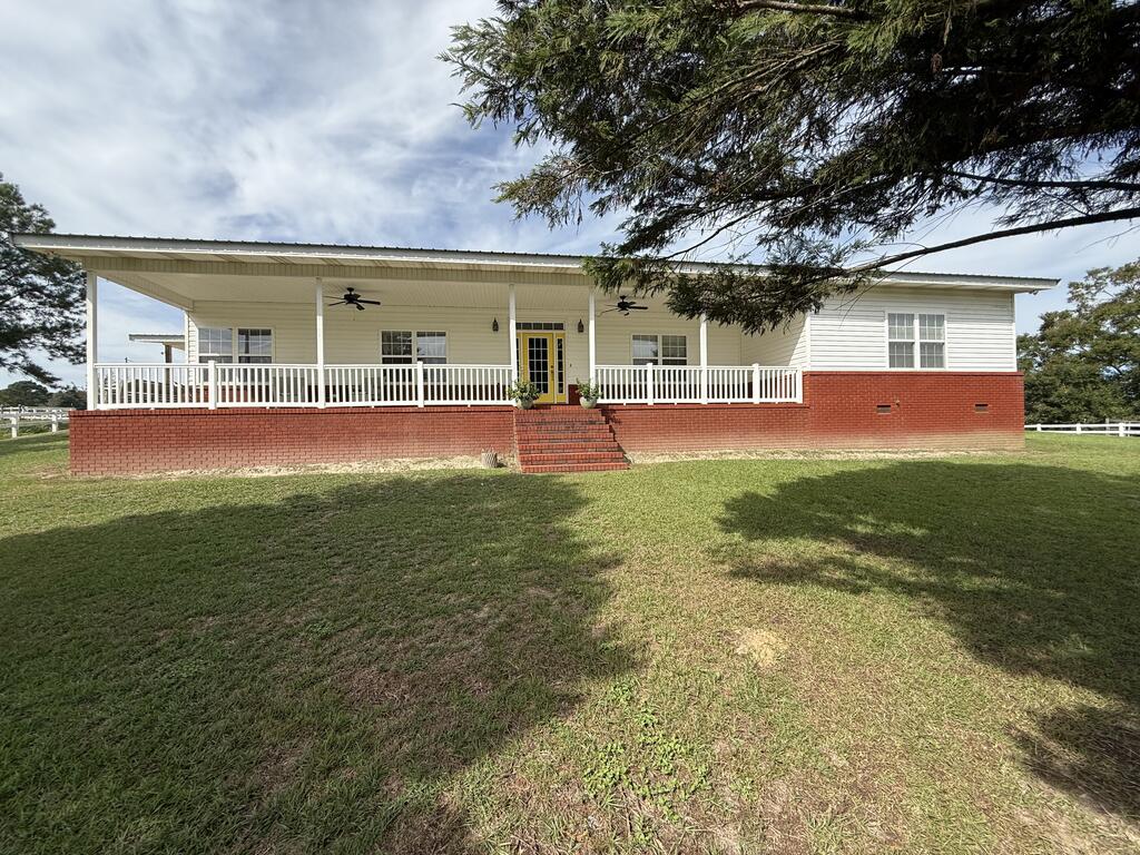 Single-story white home with a red brick base, wide covered porch, and yellow double doors.