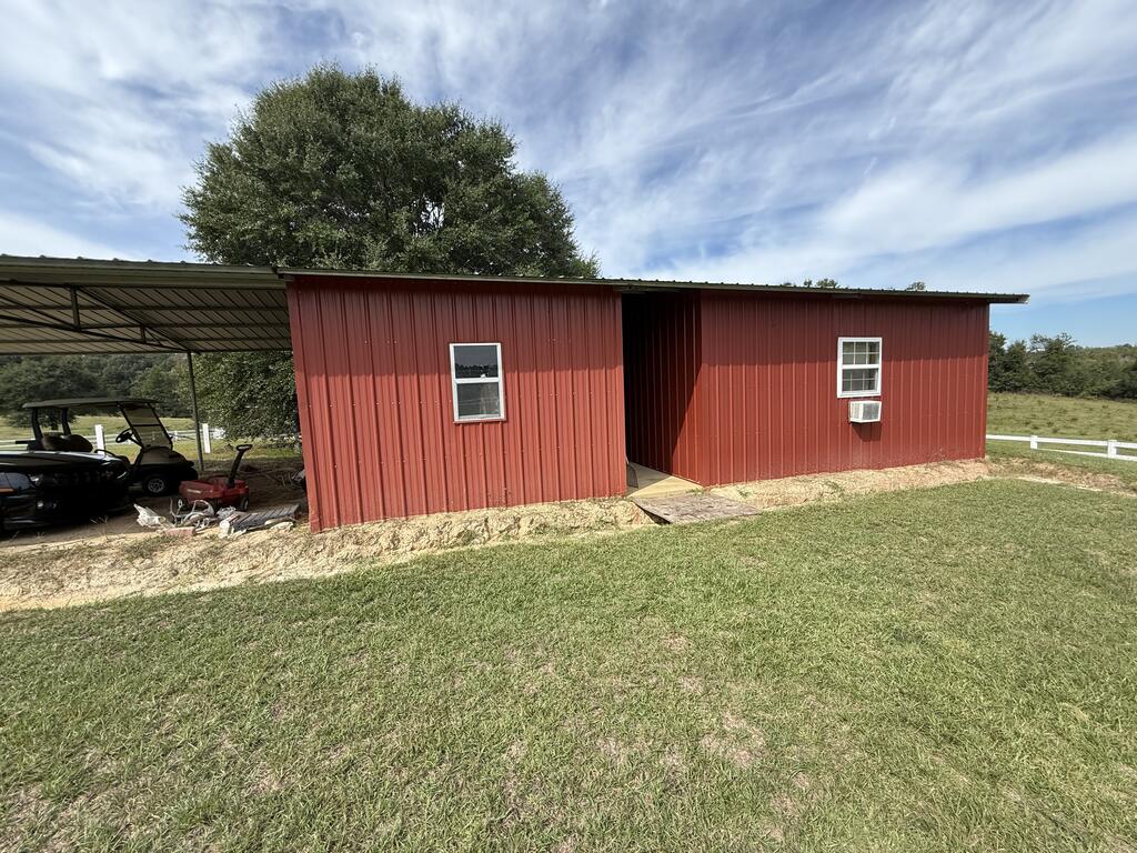 Red metal building with an attached carport and golf carts on a grassy property.