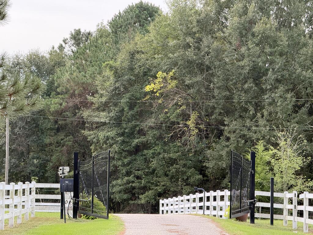 Gated gravel driveway entrance bordered by white fencing and mature trees.