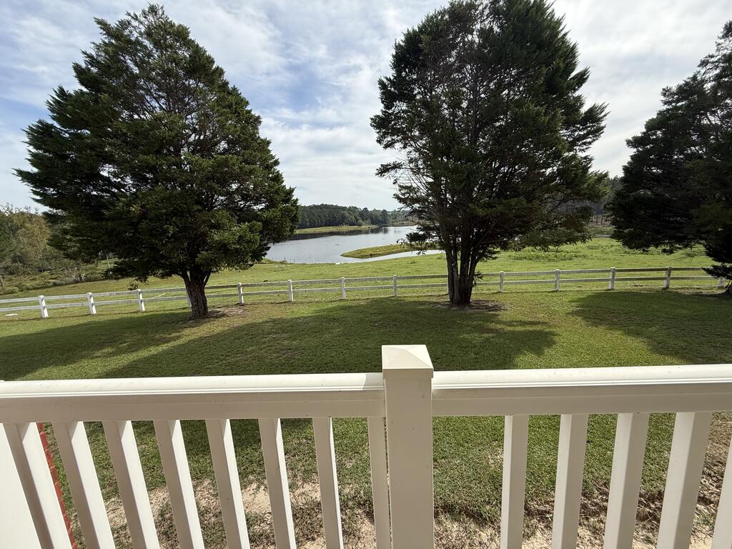 Lawn and pond beyond a white porch railing, framed by mature trees and a white fence.