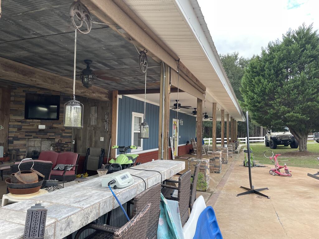 Covered patio with a stone-topped bar, outdoor seating, and hanging lanterns beside a blue-sided home.