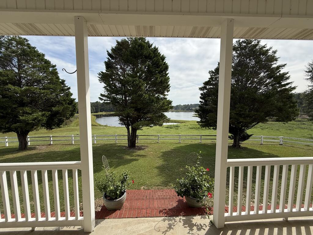 Covered porch overlooks a fenced lawn, mature trees, and a lake.