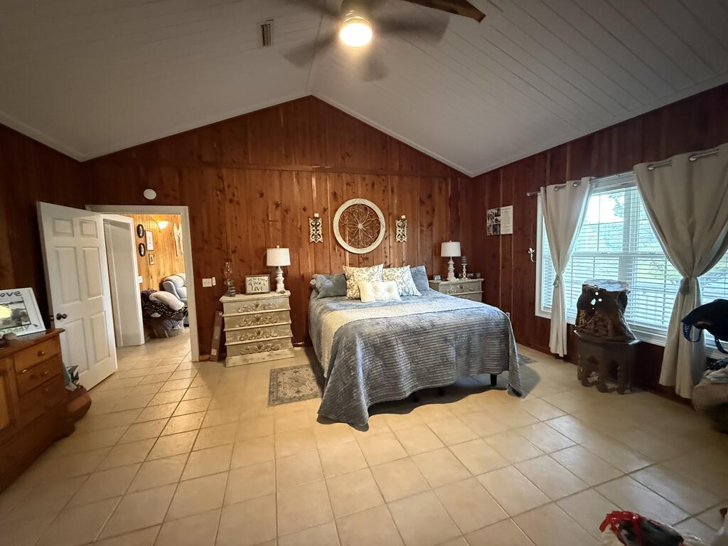 Furnished bedroom with vaulted ceiling, wood-paneled walls, and a large curtained window.