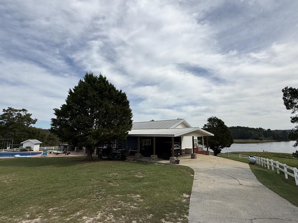 White home with a covered carport beside a lake, with a pool and curved driveway.