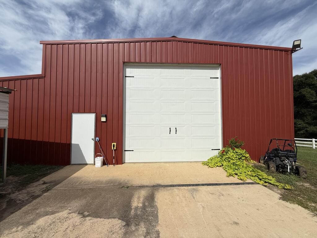 Red metal outbuilding with a large white garage door and an ATV parked beside it.