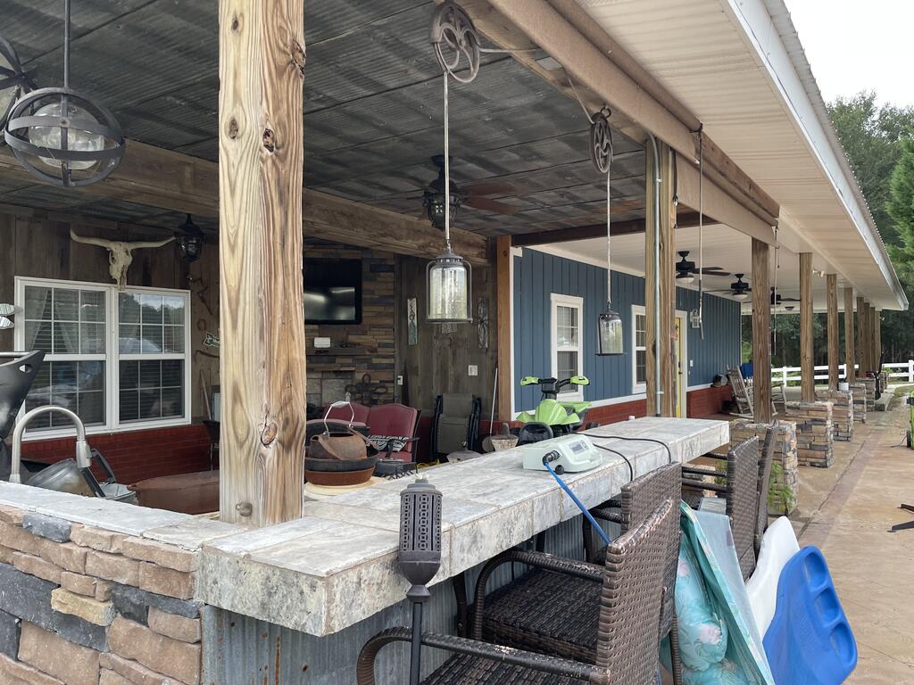 Covered patio with a long stone counter, wicker seating, and rustic timber posts.