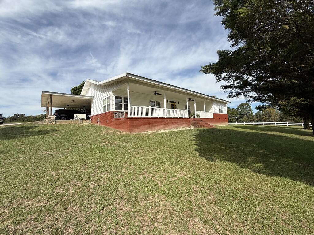 Single-story home with a wide covered porch, red brick foundation, and attached carport on a grassy lawn.