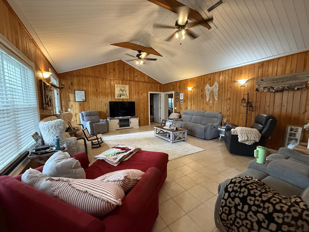 Furnished living room with wood-paneled walls, vaulted ceiling, ceiling fans, and multiple seating areas.