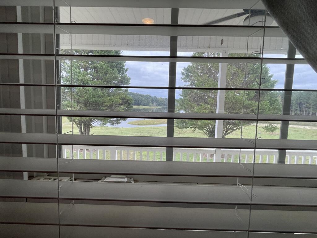 Pond and tree-lined lawn viewed through horizontal blinds from inside the home.