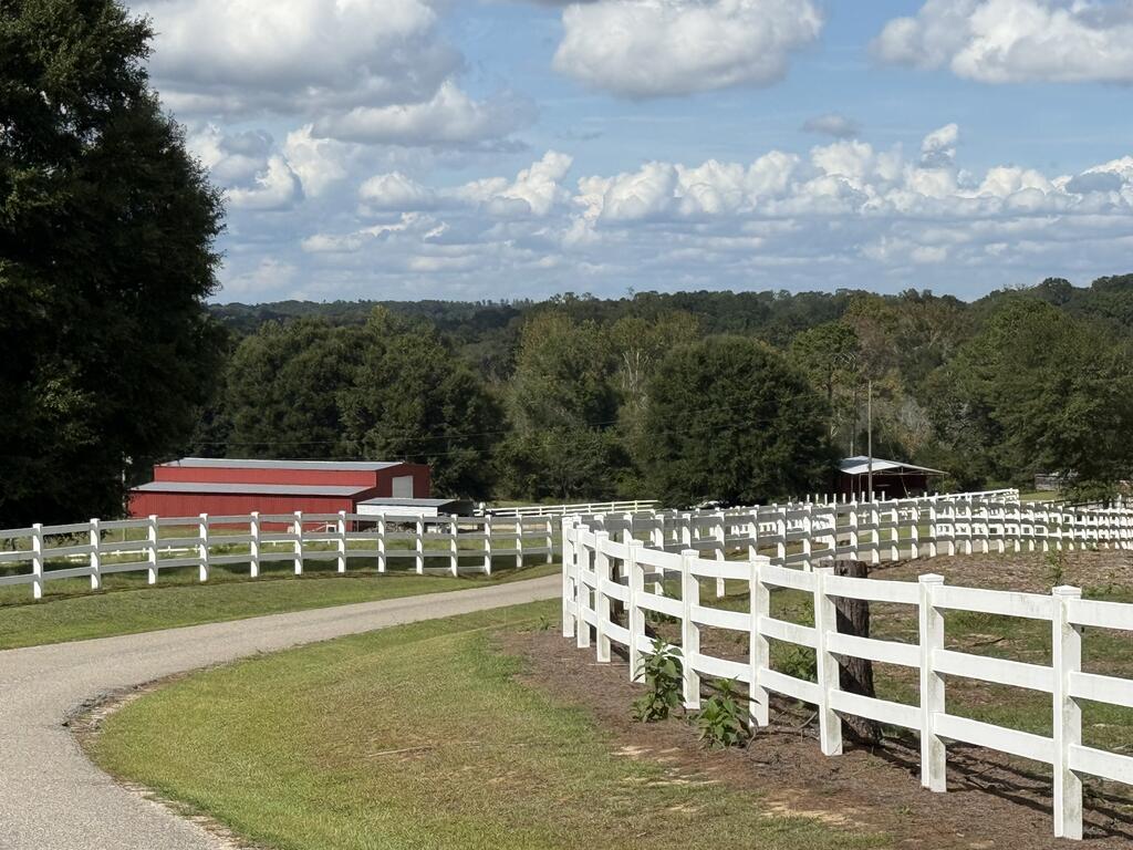 Rural property with white fencing, a red barn, grassy paddocks, and a curving driveway.