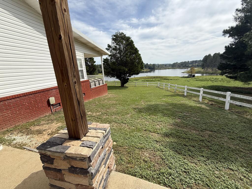 House and covered porch overlooking a grassy yard, white fence, pond, and small dock.