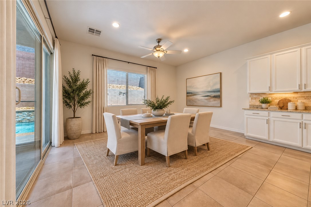 Dining area with a wood table and white chairs beside the kitchen, with a pool visible through sliding glass doors.