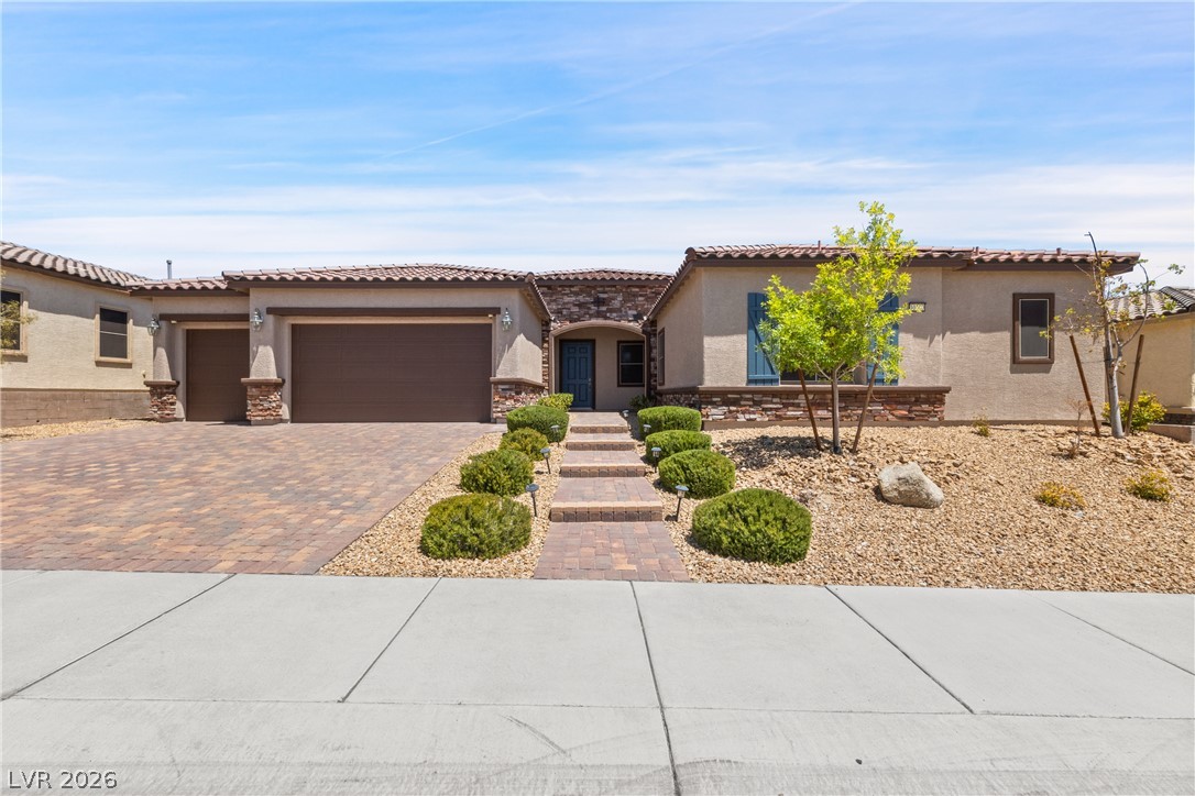 Single-story stucco home with a two-car garage, paver driveway, and desert landscaping.