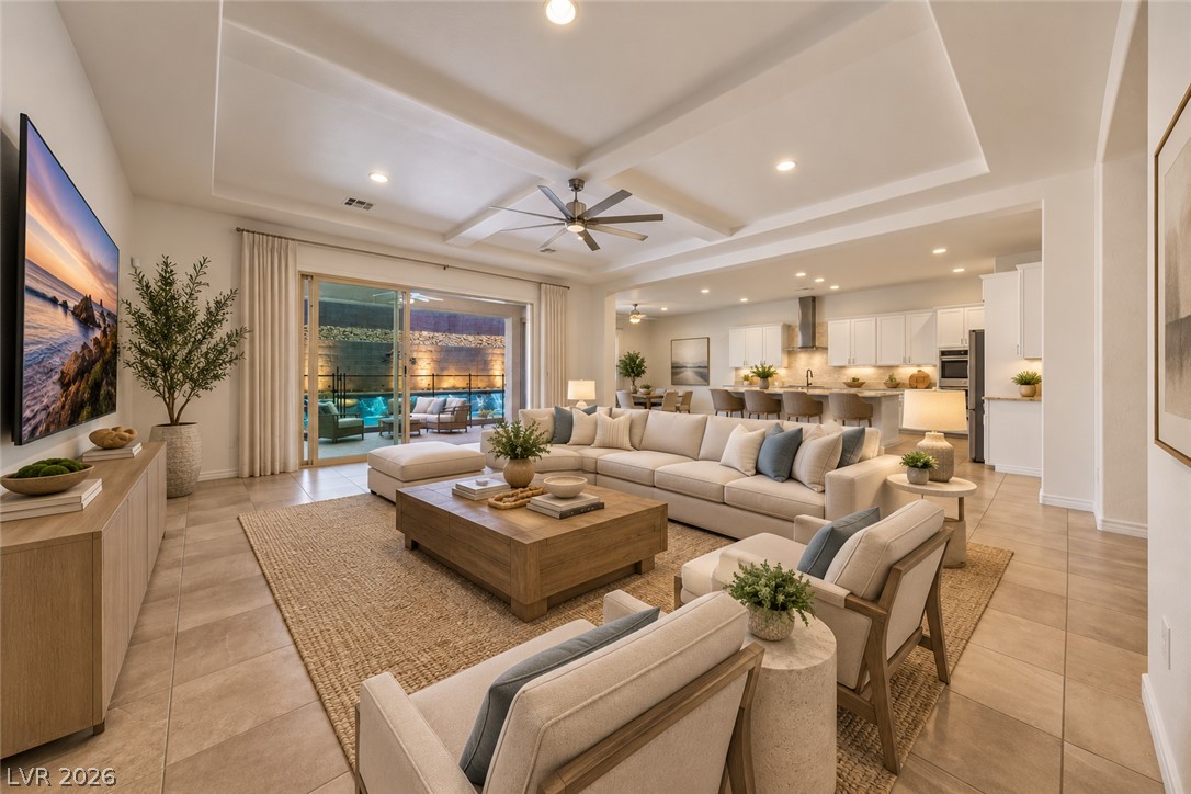 Staged living room with a cream sectional, tray ceiling, open kitchen, and sliding doors to a pool patio.