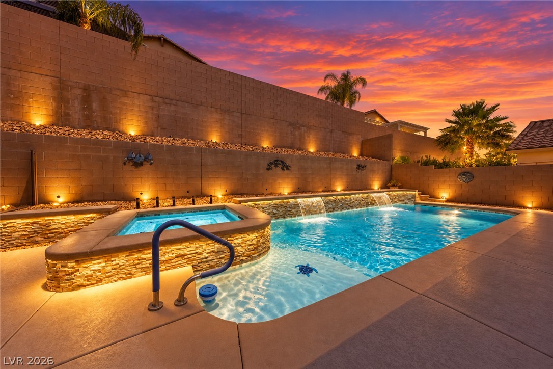 Backyard pool and raised spa with waterfalls, illuminated against a vivid sunset sky.
