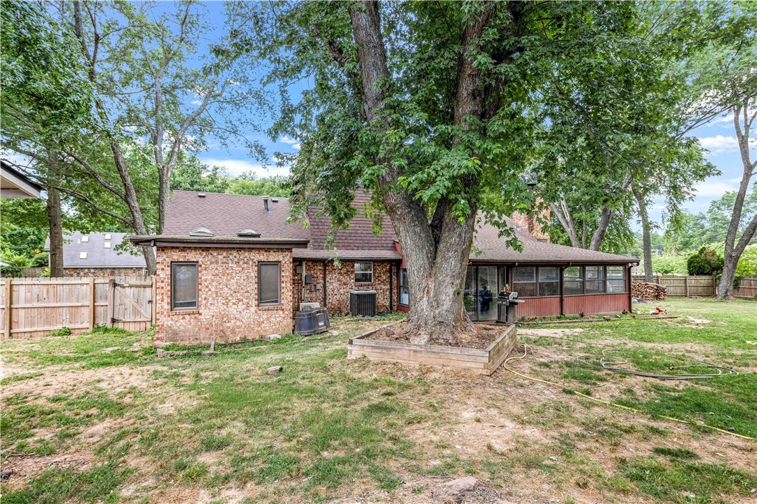 Brick home with a screened porch and fenced backyard beneath a large mature tree.