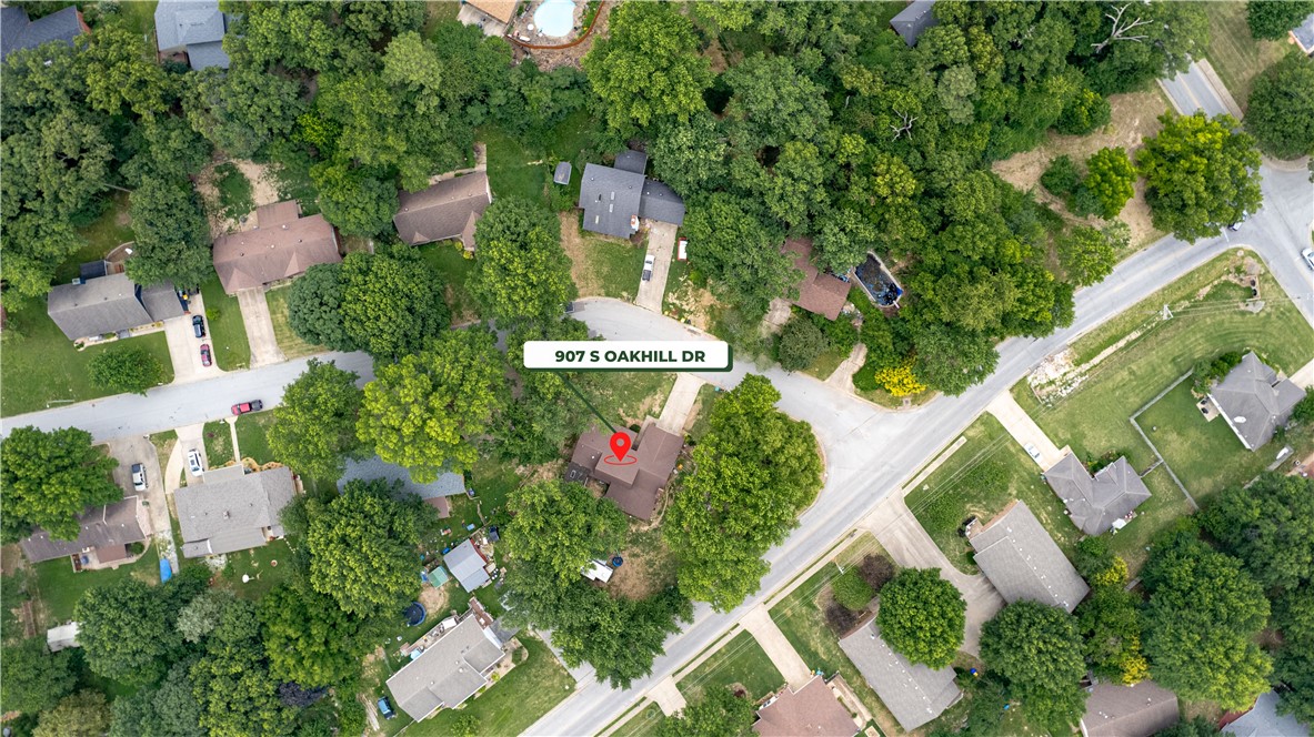 Aerial view of 907 S Oakhill Drive, a tree-surrounded home near a neighborhood intersection.