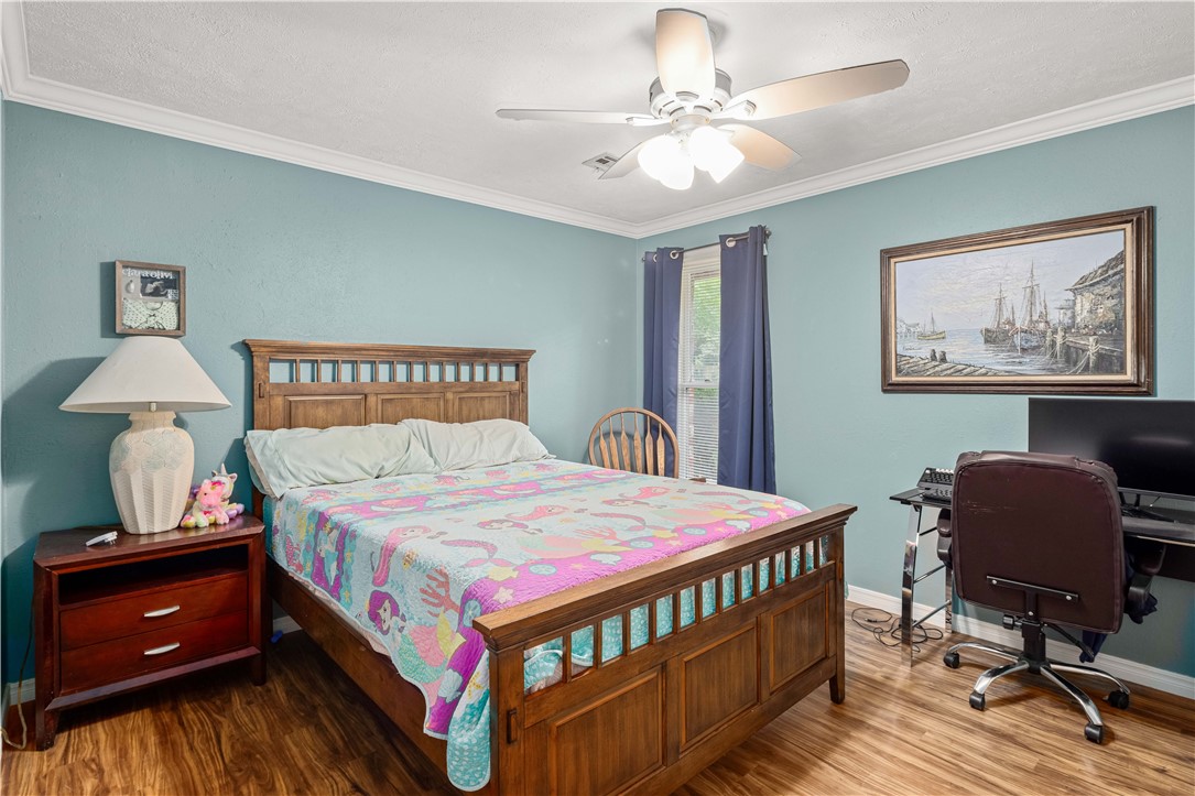 Bedroom with a wooden bed, colorful quilt, teal walls, and a desk by the window.