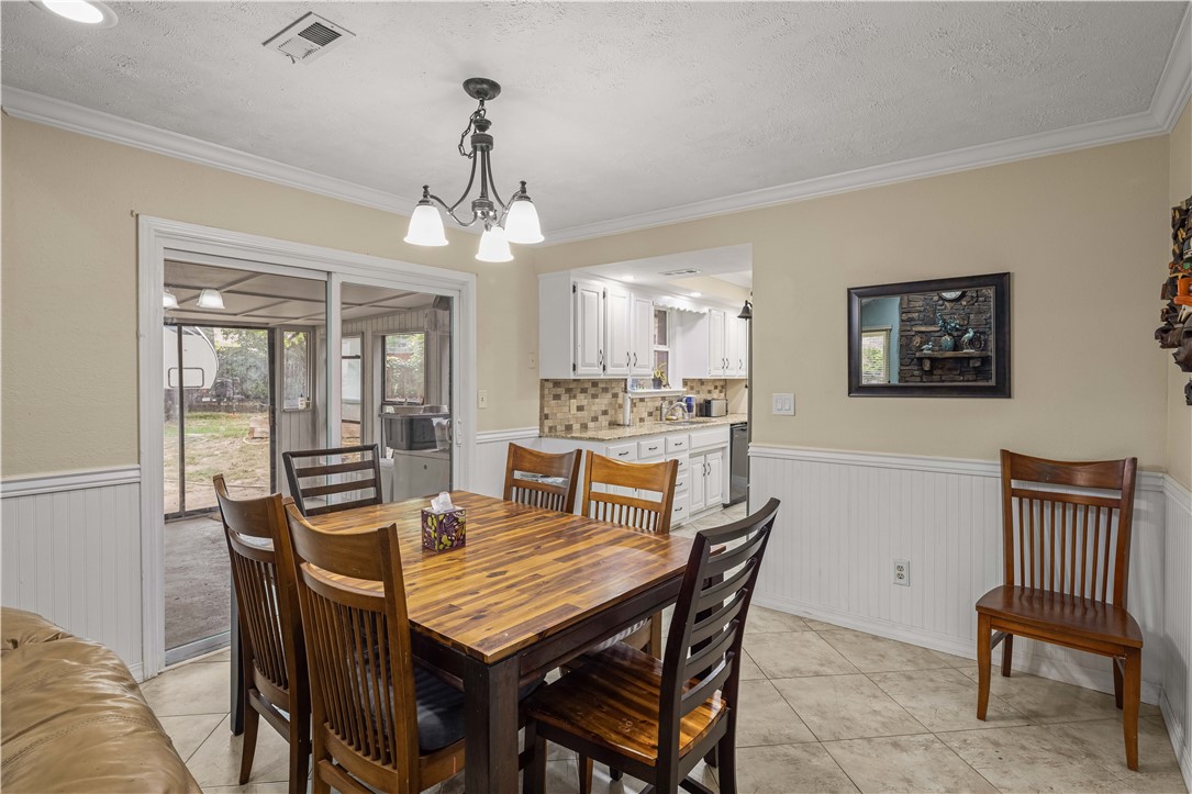Dining room with a wooden table, sliding glass doors to a covered patio, and an adjacent kitchen.