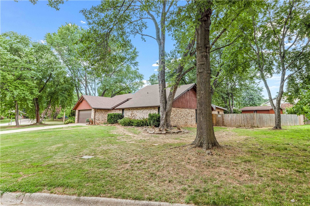 Single-story brick home with a garage, broad lawn, mature trees, and a wooden side fence.