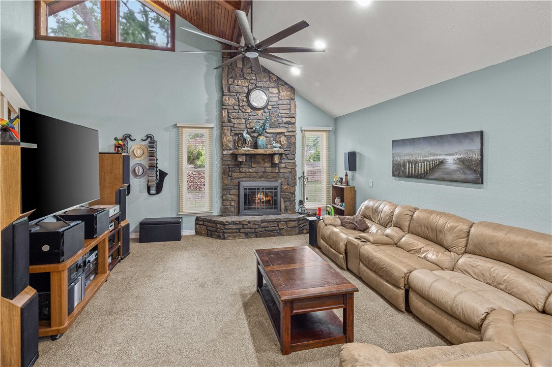 Living room with a tall stone fireplace, vaulted ceiling, and leather sectional sofa.