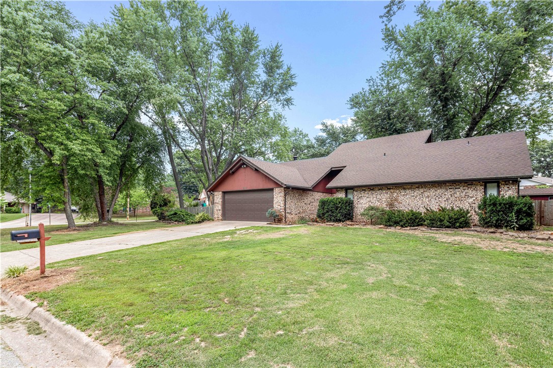 Single-story brick house with an attached garage, red gable, and mature trees.