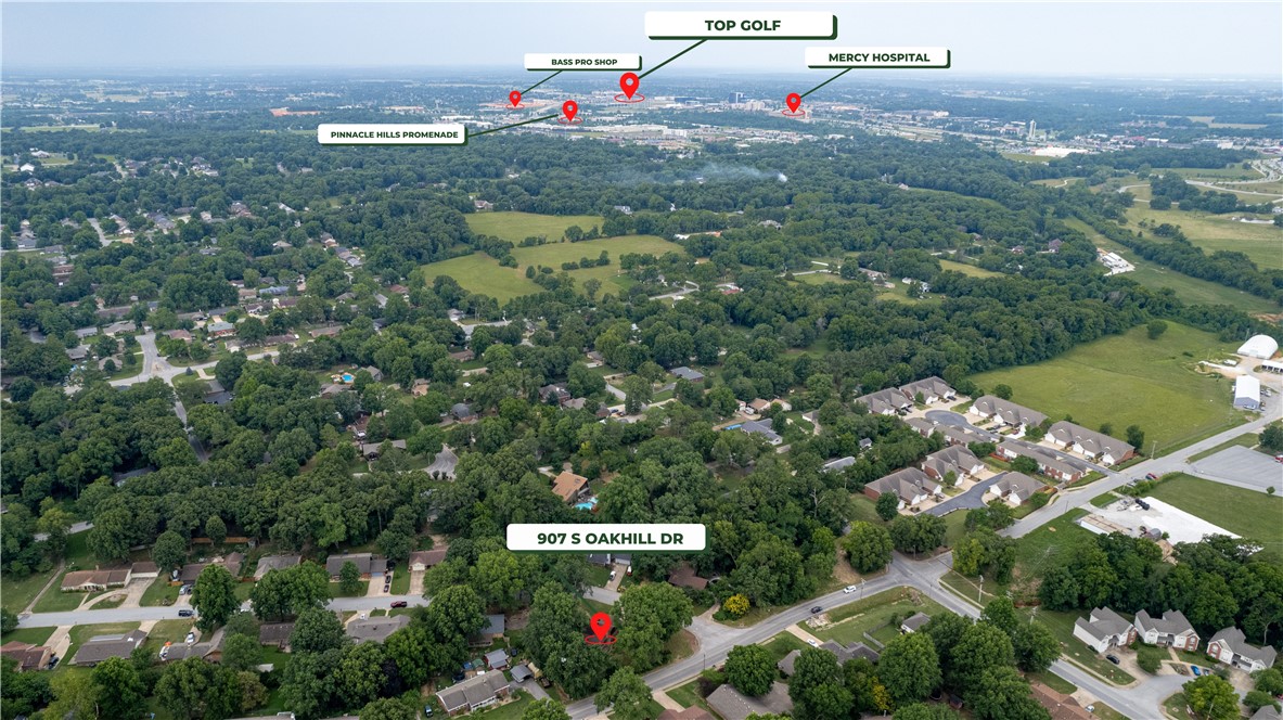 Aerial view of 907 S Oakhill Drive in a wooded neighborhood, with nearby amenities labeled in the distance.