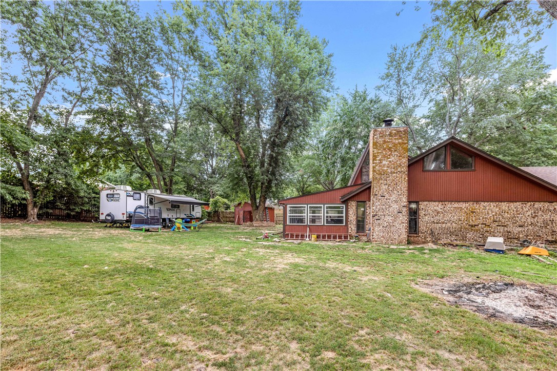 Home with a stone chimney, broad grassy yard, mature trees, and a travel trailer.