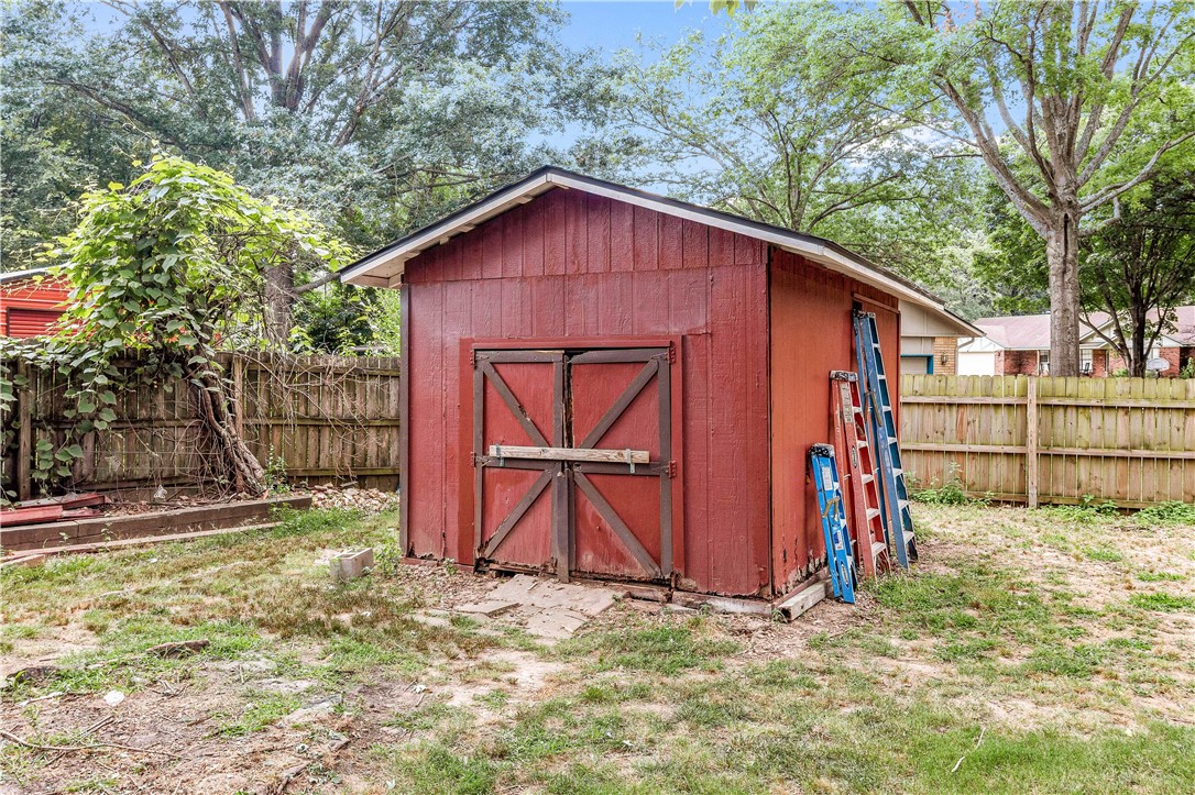 Red backyard shed with barn-style doors and ladders leaning against its side.