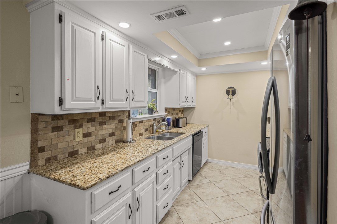 Kitchen with white cabinets, speckled granite counters, brown tile backsplash, and stainless steel appliances.