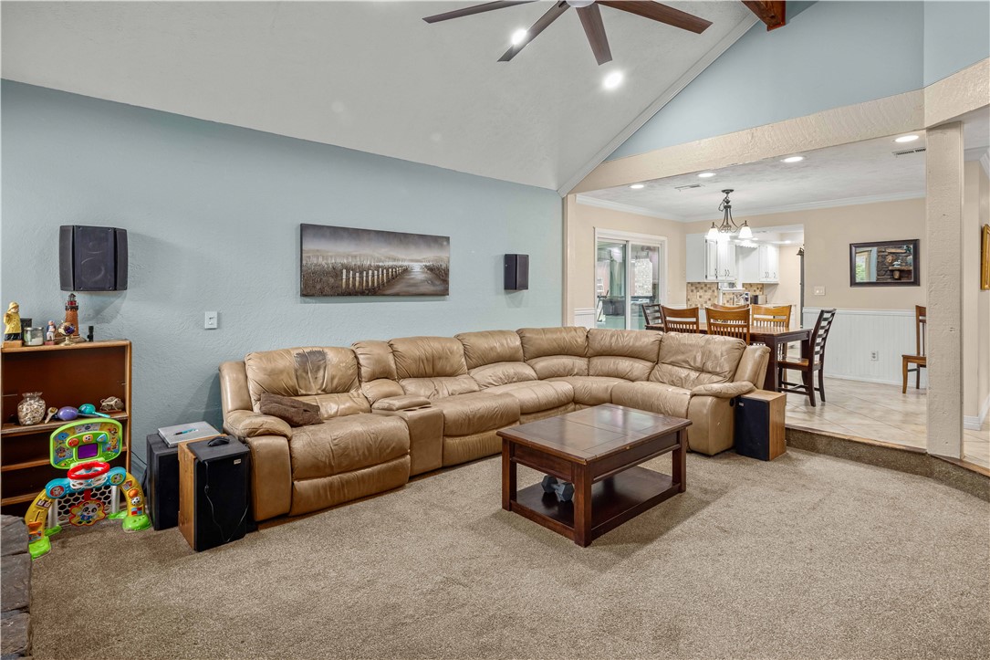 Living room with a tan leather sectional and vaulted ceiling, opening to the dining area and kitchen.