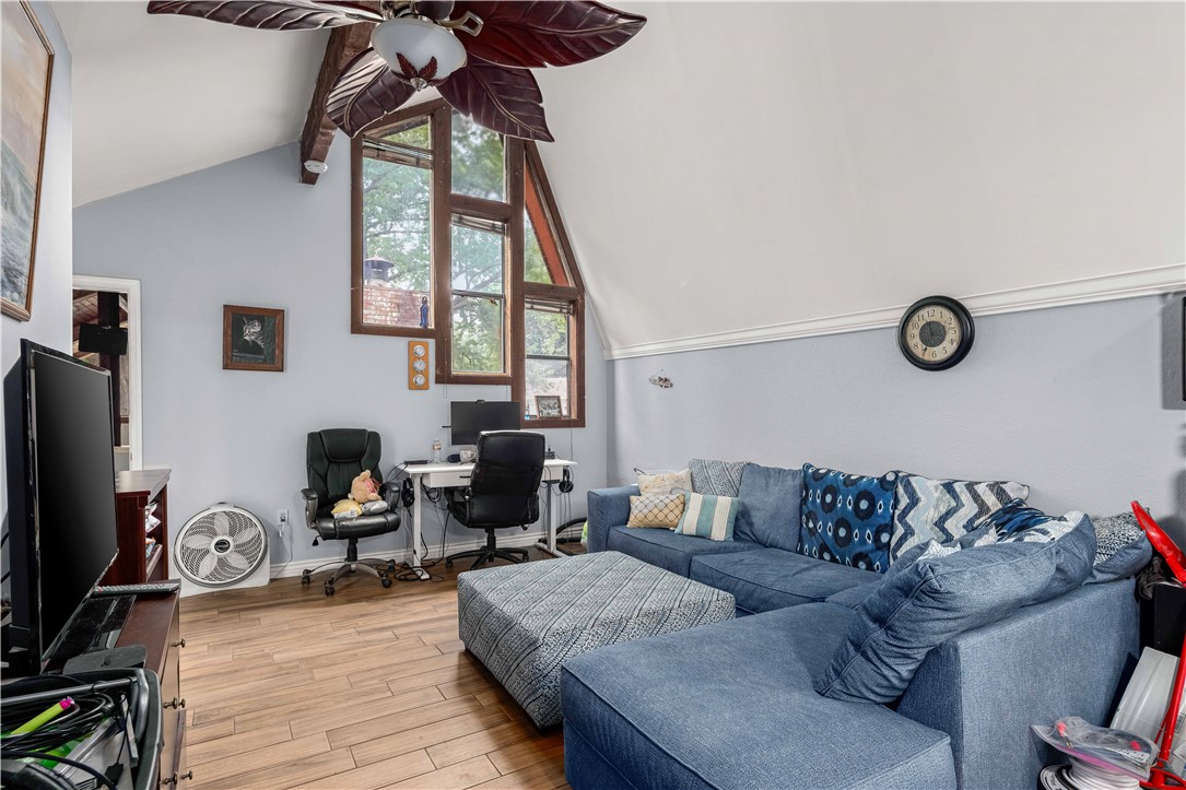 Living room with a blue sectional, patterned ottoman, vaulted ceiling, and tall wood-trimmed windows.
