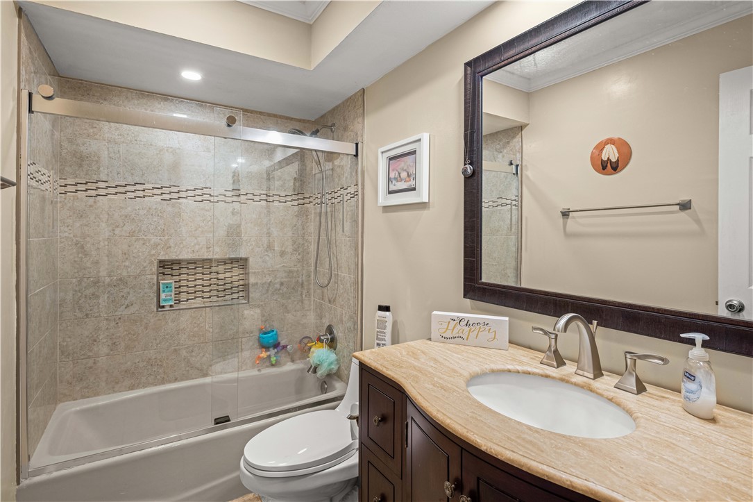 Bathroom with a tiled tub and shower, glass enclosure, and dark wood vanity.