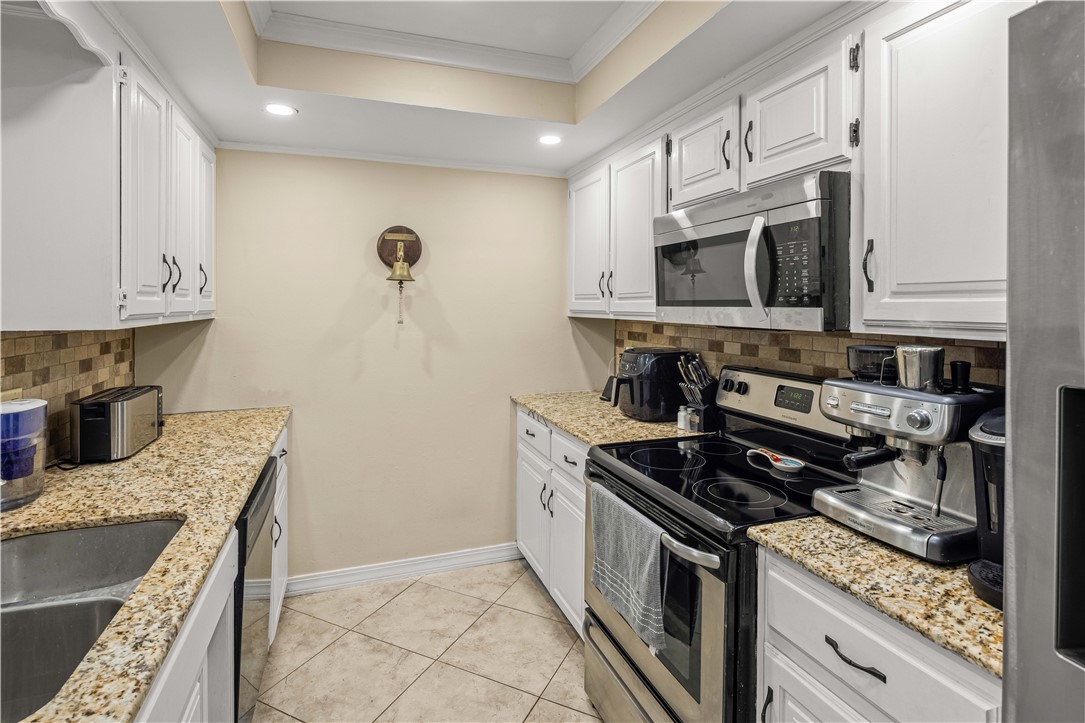 Kitchen with white cabinets, granite countertops, brown tile backsplash, and stainless steel appliances.