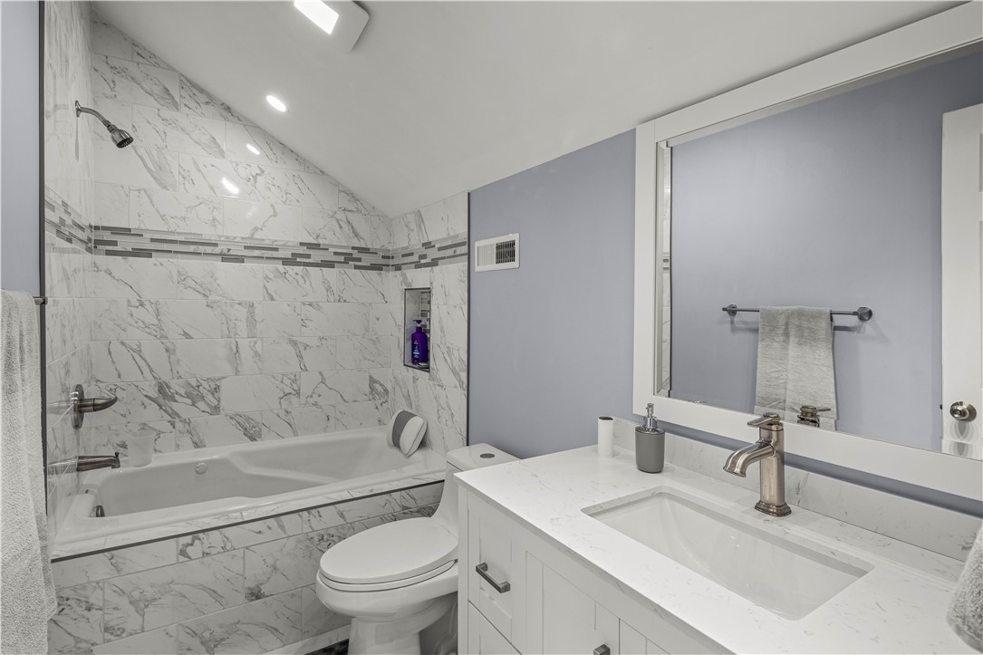 Bathroom with a marble-tiled soaking tub and white vanity with a large mirror.