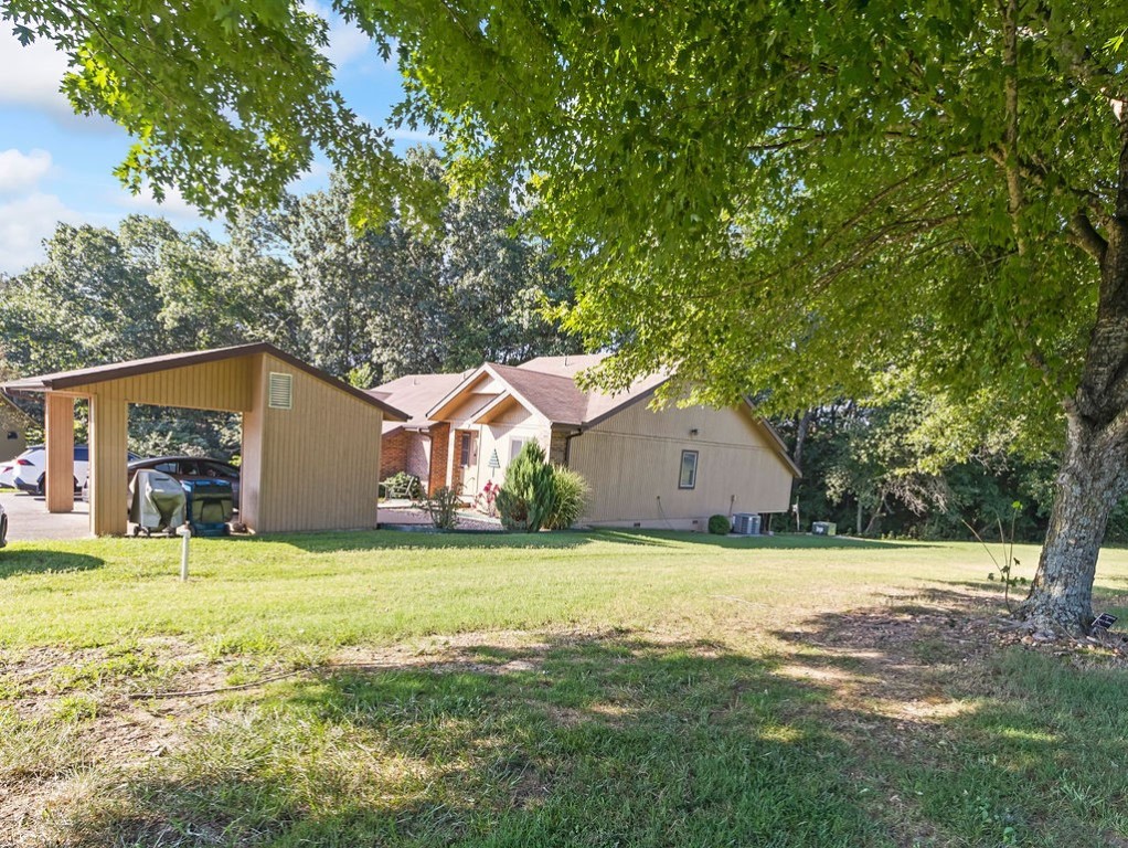 Single-story home with a detached carport and broad lawn beneath mature trees.