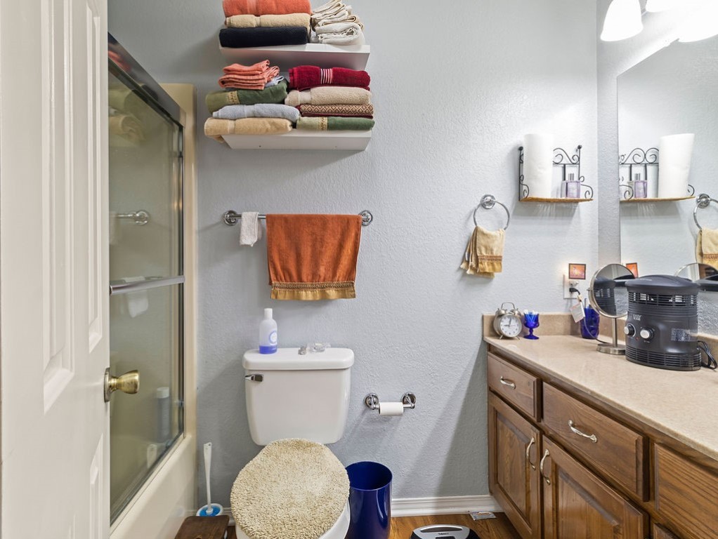 Bathroom with a glass-enclosed tub and shower, wood vanity, and shelves of folded towels.