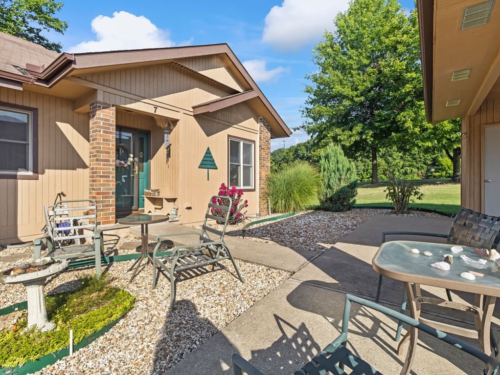 Home patio with tan siding, brick accents, outdoor seating, and landscaped gravel beds.