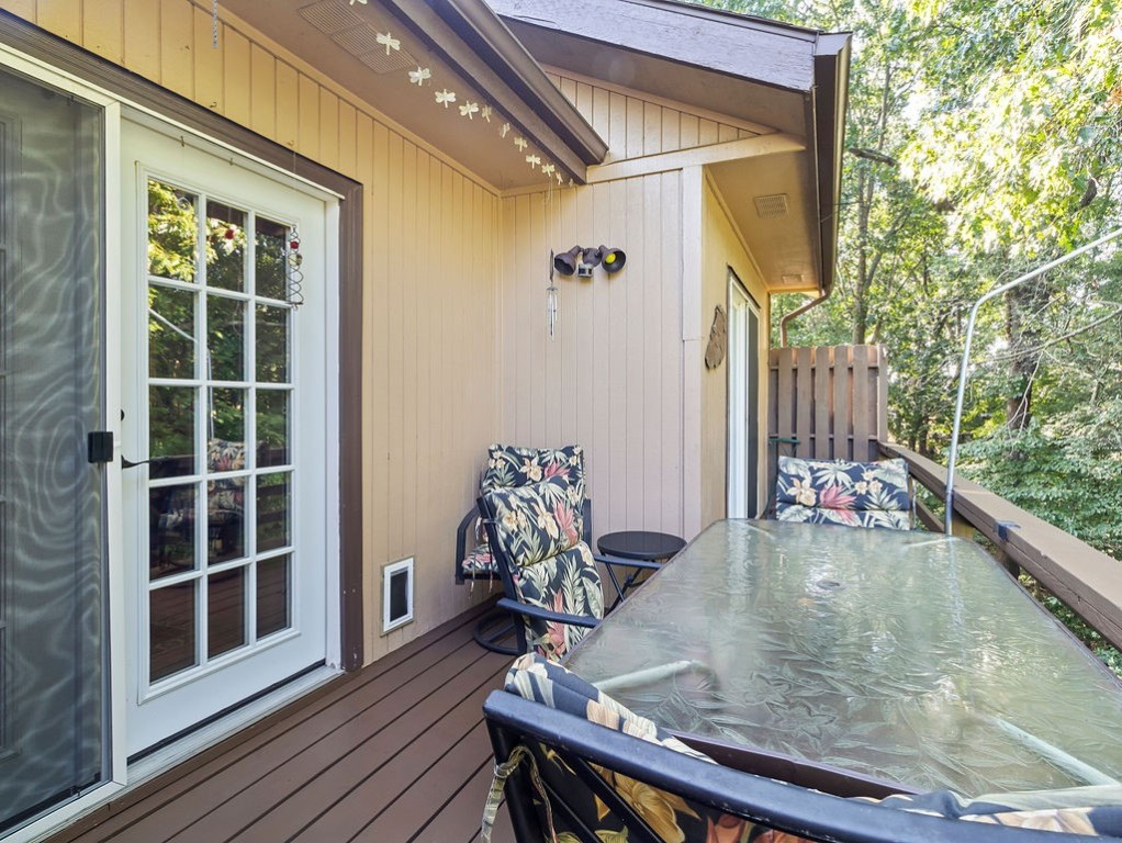 Outdoor deck with a glass-topped table and floral-cushioned chairs surrounded by trees.
