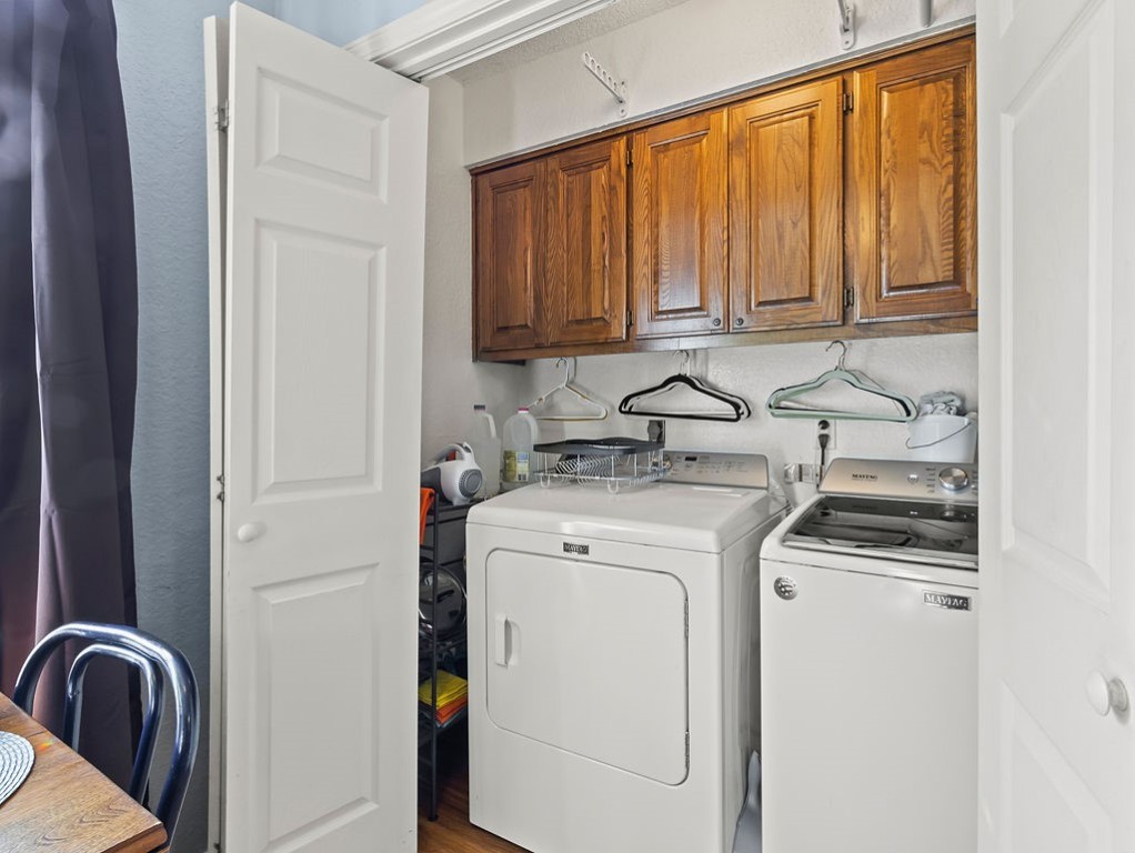 Laundry room with white Maytag washer and dryer beneath warm wood cabinets.