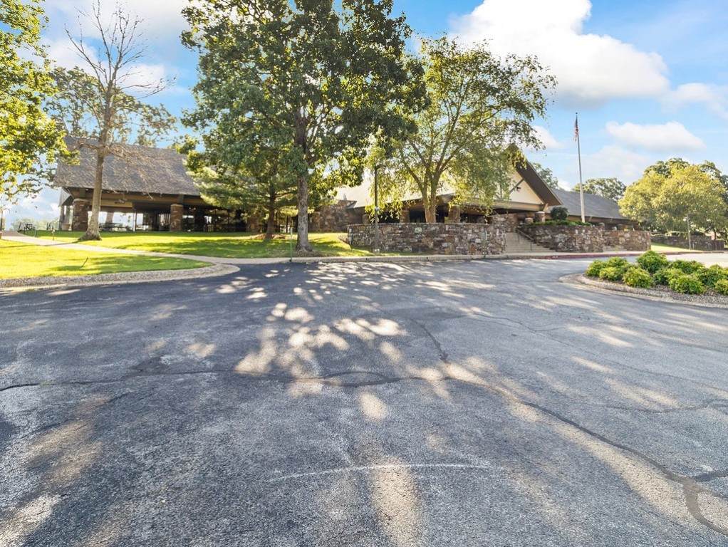 Low building behind a stone wall, shaded by mature trees, with a flagpole and paved road in front.